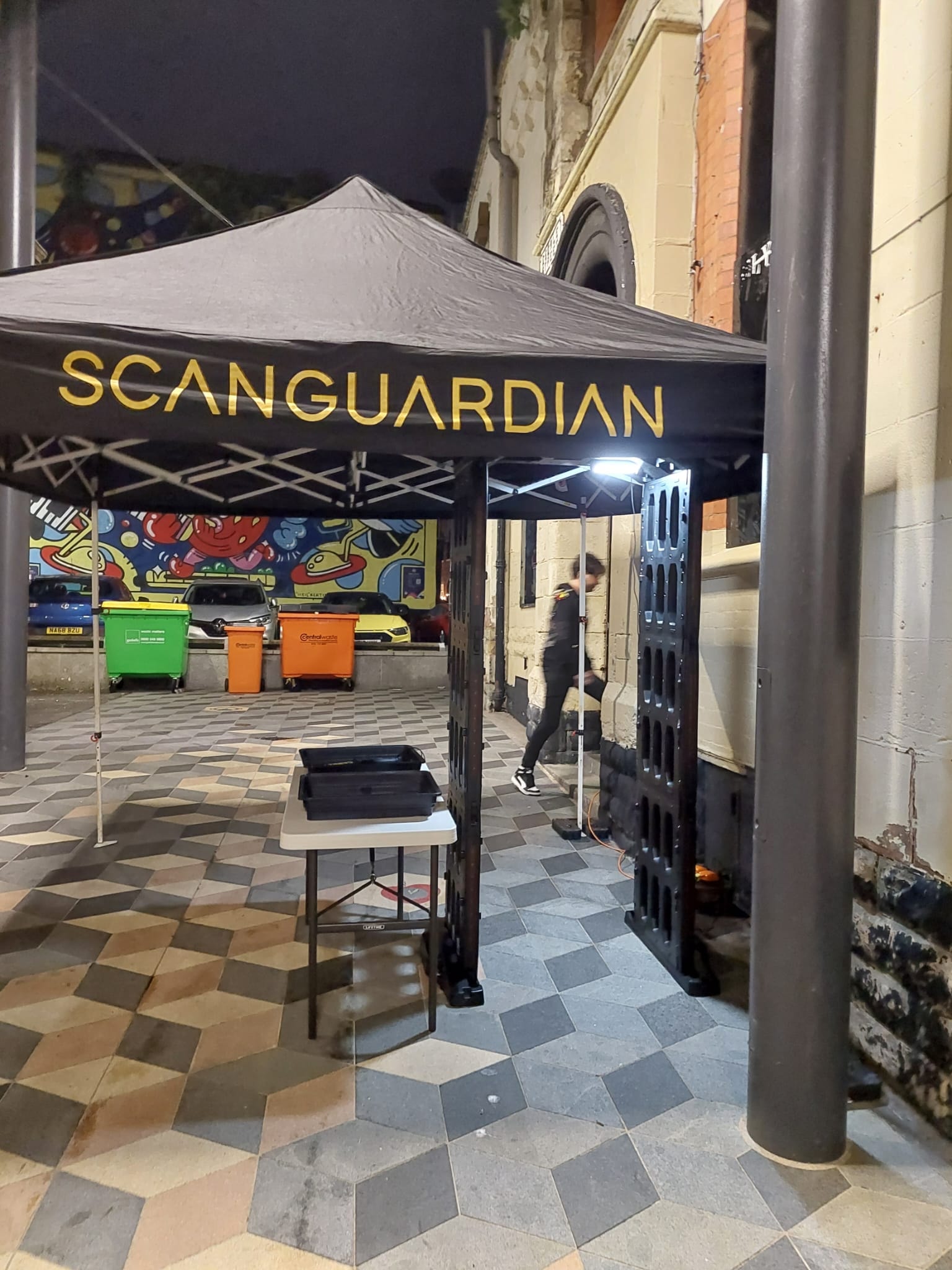 ScanGuardian branded tent with arch scanner set up outside an urban venue at night